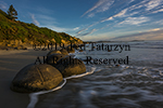 Daylight images of boulders on Moeraki beach with light whispy clouds in blue sky.